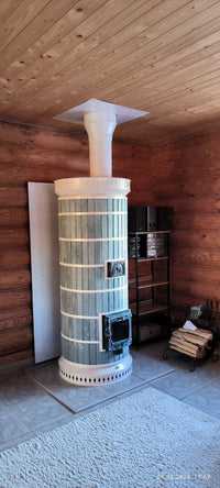 A recently assembled DIY blue Siberia masonry heater kit standing on a base in a log home under construction, showing the unit before final cleaning.