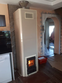 A finished Mont-Tremblant masonry heater installed in a home renovation, featuring grey tile cladding and a visible wood fire burning.