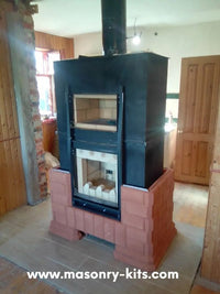 Rome model masonry heater kit under construction, featuring a red brick thermal mass base and a dedicated upper baking oven chamber for wood-fired cooking.